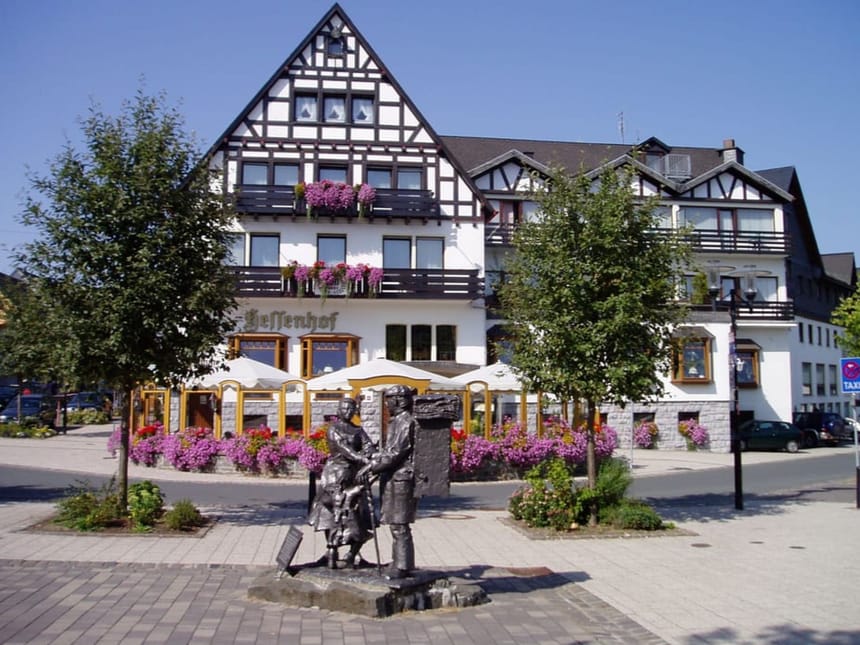 Traditionelles Fachwerkhaus mit Blumen und Skulptur im Vordergrund.