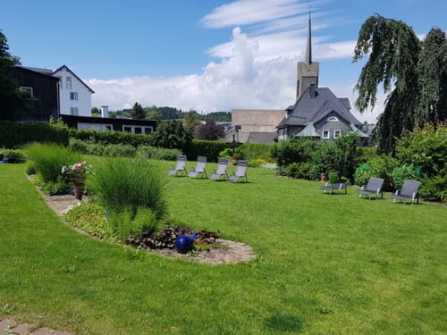 Gepflegte Gartenanlage mit Liegestühlen und einer Kirche im Hintergrund.