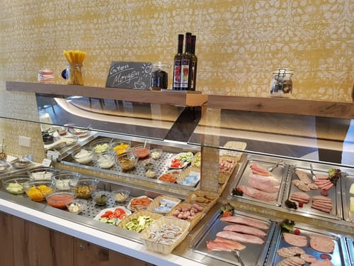 Frühstücksbuffet mit verschiedenen Aufschnittsorten, frischem Gemüse und Beilagen.