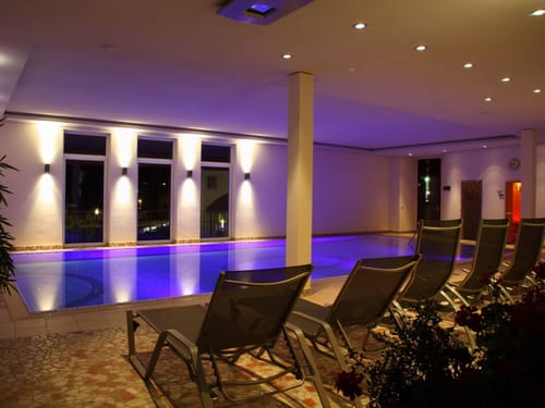Entspannungsbereich mit beleuchtetem Innenpool und Liegestühlen in einem Spa.