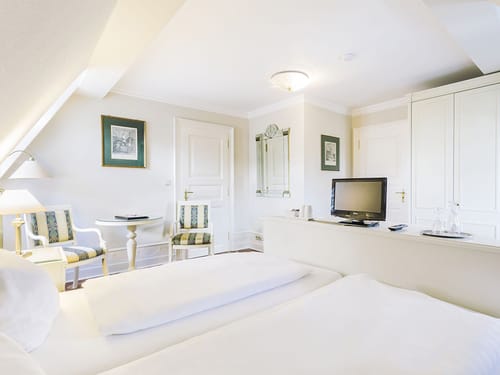 gräumiges Doppelzimmer mit Doppelbett, zwei Sesseln, Tisch, Wandschrank und TV