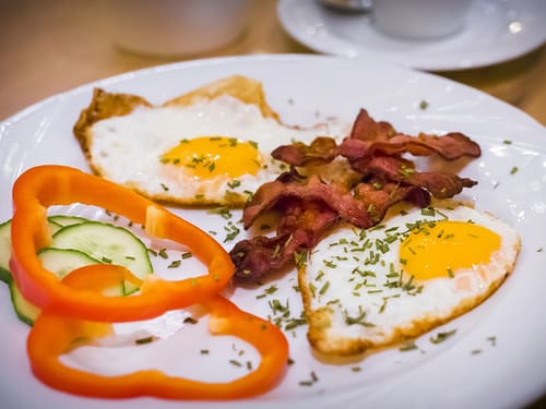 Frühstücksteller mit Spiegelei, Speck, Paprika und Gurke