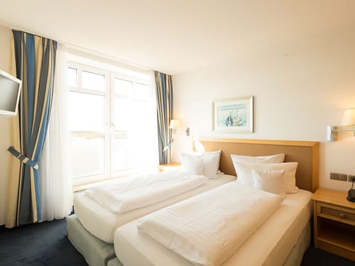 hell und modern eingerichtetes Doppelzimmer mit Doppelbett, Leselampen und TV