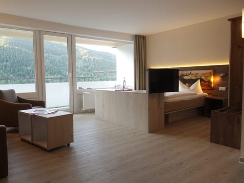 Zweitbettzimmer mit Doppelbett, TV, Sessel, Couch, Tisch, Panoramafenster und Balkon