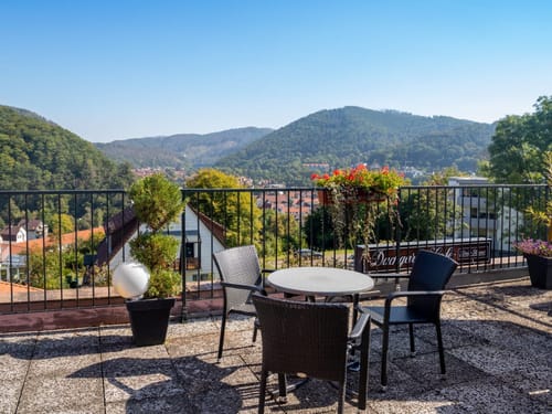 Terrasse mit Panoramablick auf bewaldete Hügel und ein Dorf.