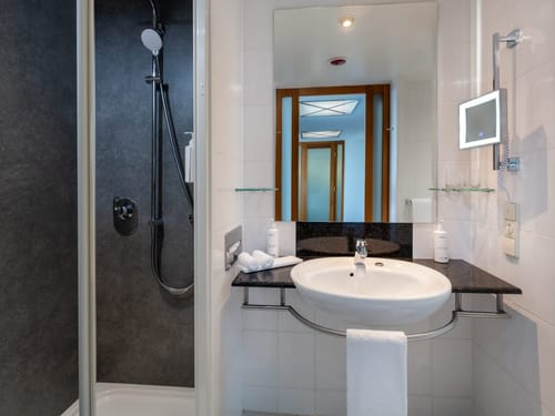 Gepflegtes Hotelbadezimmer mit moderner Regendusche, rundem Waschbecken