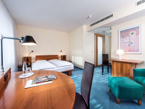 Stilvolles Hotelzimmer mit Doppelbett, Holzmöbeln und türkisfarbenem Sessel