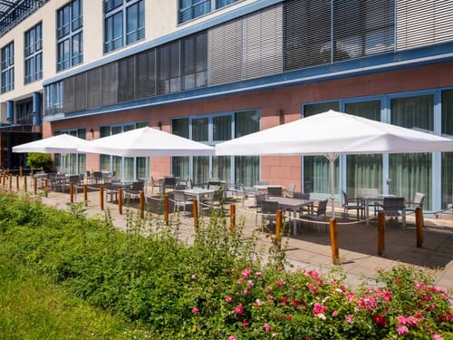 Die einladende Hotelterrasse bietet schattige Sitzplätze unter weißen Sonnenschirmen