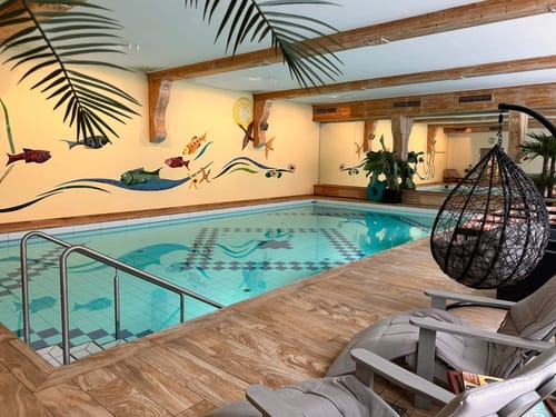Gemütlicher Innenpoolbereich mit buntem Wandbild und Hängesessel.
