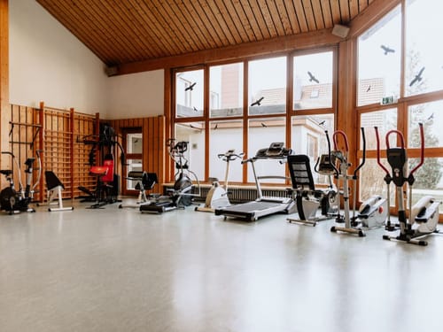 Heller Fitnessraum mit verschiedenen Fitnessgeräten und großen Fenstern