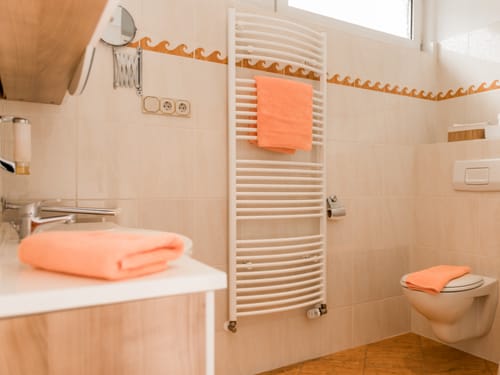Modernes Badezimmer mit Handtuchheizkörper und orangefarbenen Handtüchern.