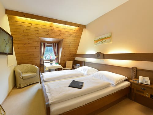 einfaches Doppelzimmer mit Doppelbett, Tisch, Sessel und Stuhl