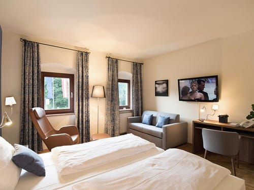 modernes Doppelzimmer mit Doppelbett, Couch, Sessel, Stehlampe, Schreibtisch und Stuhl