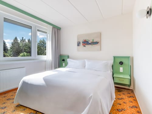 Helles und gemütliches Hotelzimmer mit Doppelbett und großem Fenster mit Blick ins Grüne.
