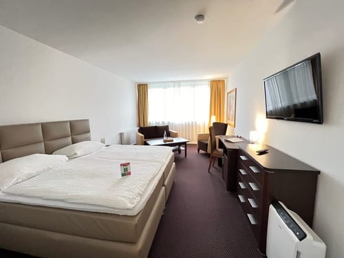 Boxspringbett, zwei Sessel, TV und Sideboard im Doppelzimmer