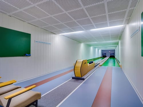 Moderne Kegelbahn mit grüner Spielfläche und Sitzgelegenheiten.