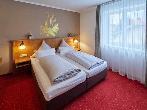 Gemütliches Doppelzimmer mit Holzverkleidung und rotem Teppichboden in einem Hotel