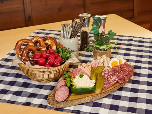 Bayerische Brotzeit mit Brezeln, Wurst und Radieschen auf kariertem Tischtuch