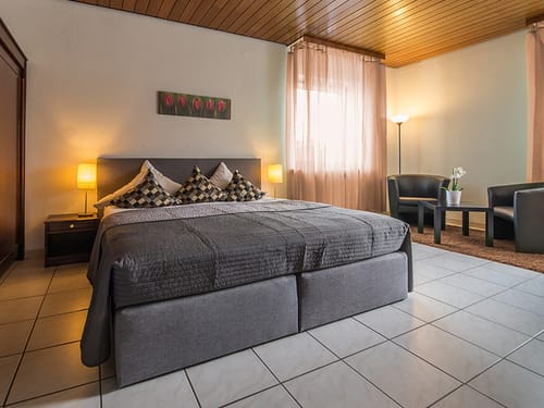 Boxspringbett, zwei Sessel, Tisch und Kleiderschrank im Hotelzimmer