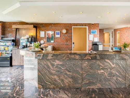 Der repräsentative Marmorempfangstresen im Hotelfoyer mit Coffee-Corner und Backsteinwand-Ambiente lädt Gäste herzlich willkommen