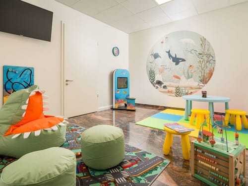 Einladendes Kinderspielzimmer mit Unterwasserwelt-Wandbild, Dinosaurier-Sitzsack und vielfältigem Spielzeug für kleine Gäste