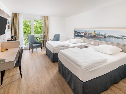 Komfortables Hotelzimmer mit zwei Einzelbetten, stimmungsvollem Hafenpanorama-Wandbild und sonnigem Balkon mit Grünblick