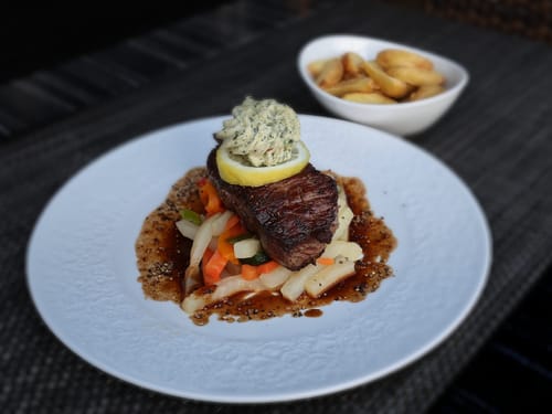 Zartes Rindersteak mit Kräuterbutter, sautiertem Saisongemüse und Bratenjus – ein klassisches Restaurantgericht mit Bratkartoffeln als Beilage.