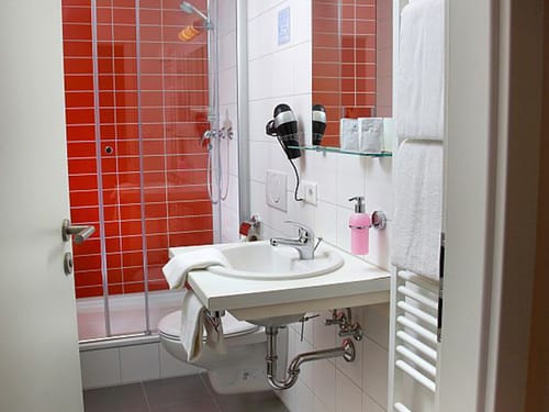 Badbereich mit roten Kacheln, Dusche, Waschtisch und Spiegel