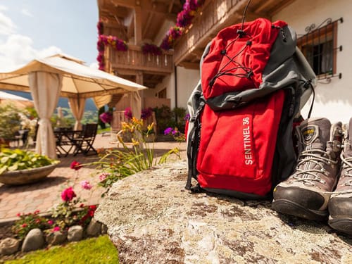 Terrasse mit Pavillon, Garten Stühlen, Tischen und einem Rucksack und Wanderschuhen im Vordergrund