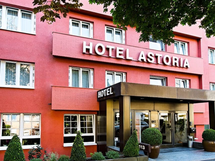 Eingangsbereich des Hotel Astoria mit roter Fassade und gepflegter Begrünung