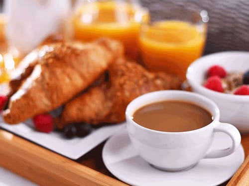 Frühstückstablett mit Croissants, Orangensaft, Müsli und einer Tasse Kaffe