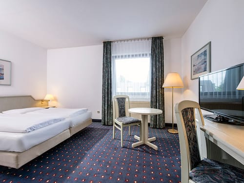 Doppelzimmer mit Twinbett, Stühlen, Tisch, Stehlampe, Schreibtisch und TV