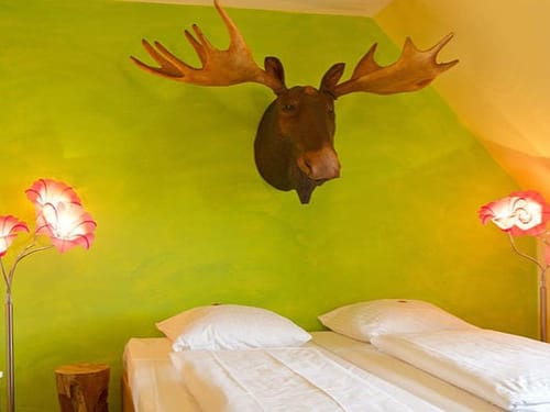 Einzigartig dekoriertes Schlafzimmer mit grün gestrichener Wand, Elchkopf und stilvollen Blumenlampen.