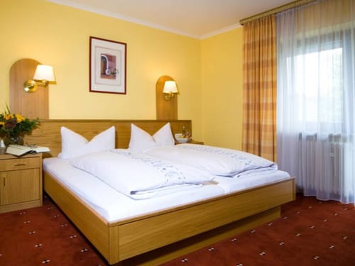 Gemütliches Hotelzimmer mit Doppelbett, warmen Farben und Fenstervorhängen.