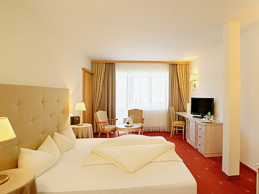 Doppelzimmer Classis mit Boxspringbett, Stühlen, Tisch, TV und Sideboard