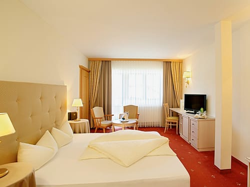 Doppelzimmer Classis mit Boxspringbett, Stühlen, Tisch, TV und Sideboard