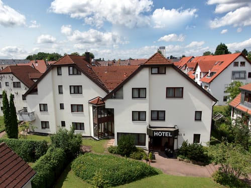 Außenansicht eines gemütlichen Hotels umgeben von gepflegten Gärten und roten Dächern.
