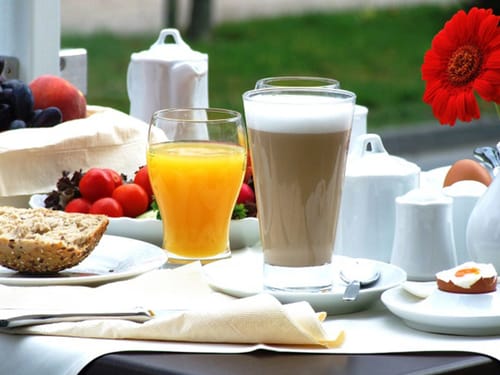 gedeckter Frühstückstisch mit Saft, Kaffee, Ei und Brötchen