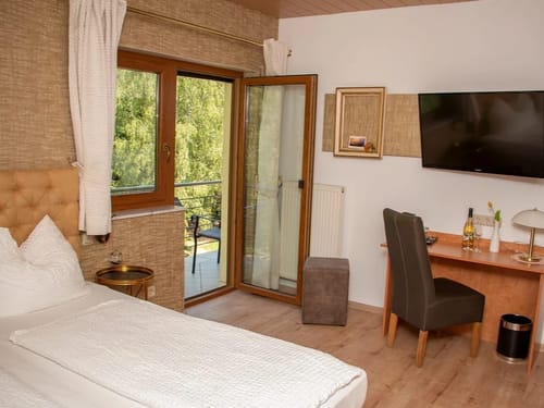 großzügiges Doppelzimmer mit Doppelbett, Schreibtisch, Stuhl, TV und Balkon