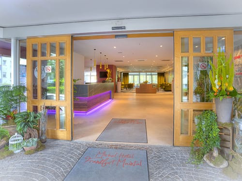 Eingang mit Pflanzen im Vordergrund und Schiebetüren in Holzoptik