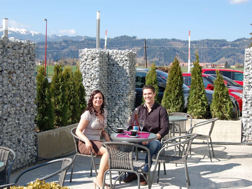 Paar sitzt im Freien auf Terrasse eines Cafés mit Bergblick.
