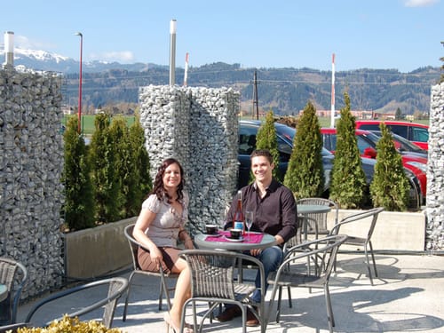 Paar sitzt im Freien auf Terrasse eines Cafés mit Bergblick.