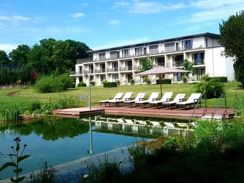 Modernes Hotel mit Naturteich und Liegestühlen im Garten.