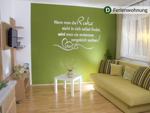 Gemütliches Wohnzimmer einer Ferienwohnung mit grüner Akzentwand und inspirierendem Zitat.