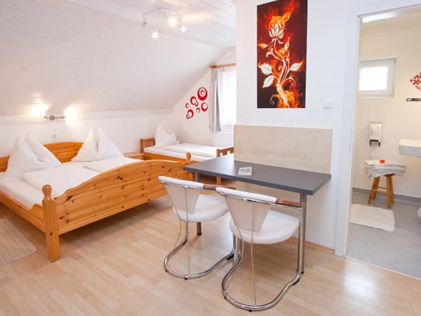 Gemütliches Gästezimmer mit Doppel- und Einzelbett, Holzmöbeln, Tisch mit Stühlen und angrenzendem Badezimmer.