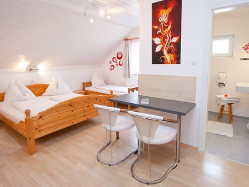 Gemütliches Gästezimmer mit Doppel- und Einzelbett, Holzmöbeln, Tisch mit Stühlen und angrenzendem Badezimmer.