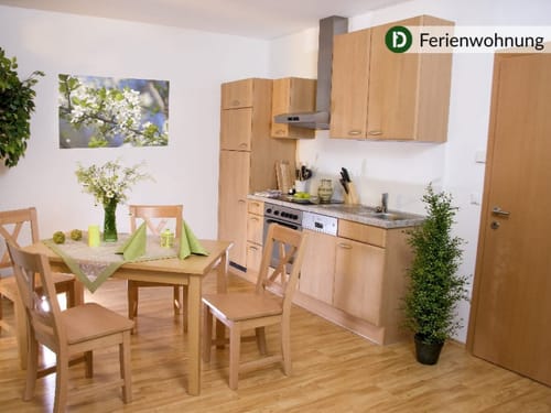 Gemütliche Küche in einer Ferienwohnung mit Esstisch und Stühlen, umgeben von Holzmöbeln und grüner Dekoration.