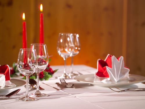 Elegant gedeckter Tisch mit Weingläsern und entzündeten roten Kerzen.