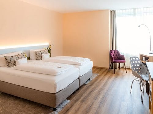 Modern eingerichtetes Hotelzimmer mit Doppelbett, Schreibtisch und gemütlichem Sessel am Fenster.