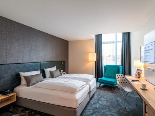 Standard Zimmer mit Twinbett, großem Sessel, Schreibtisch, Stuhl und Stehlampe